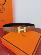 Reversible leather belt with tan strap and gold H buckle on orange box, dark side inside