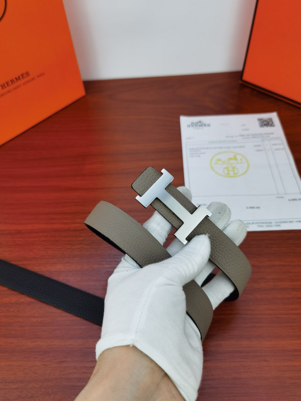 Hermes belt with light gray leather strap and gold-tone H buckle held by glove