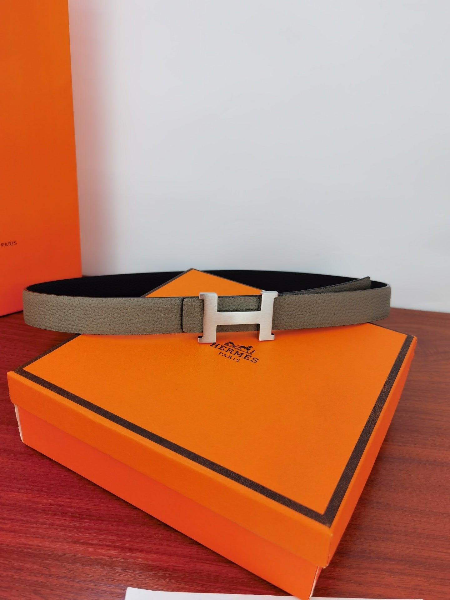 Hermes belt on orange box, light gray strap with gold-tone H buckle