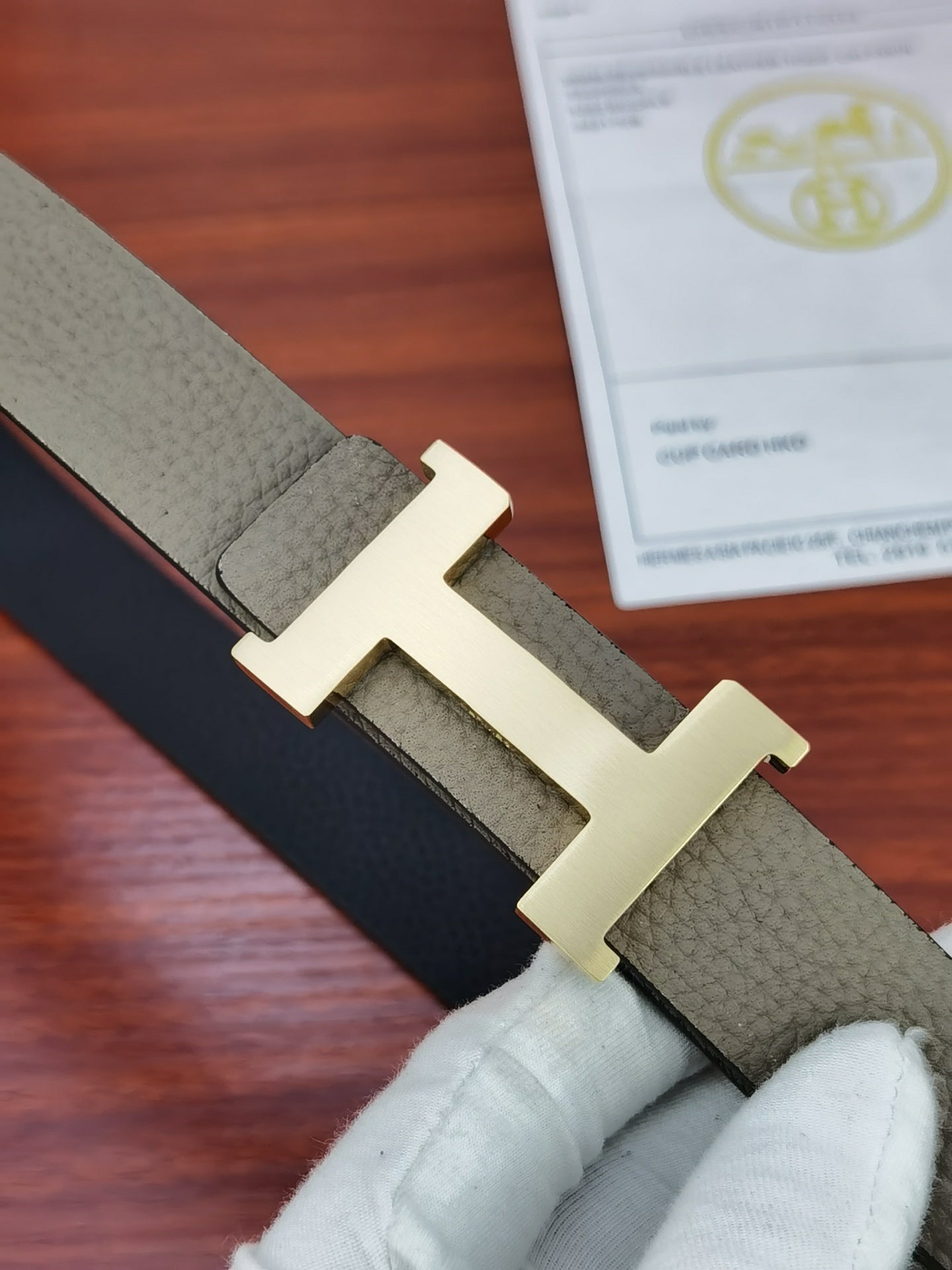 Hermes belt close-up of gold-tone H buckle on light gray leather strap