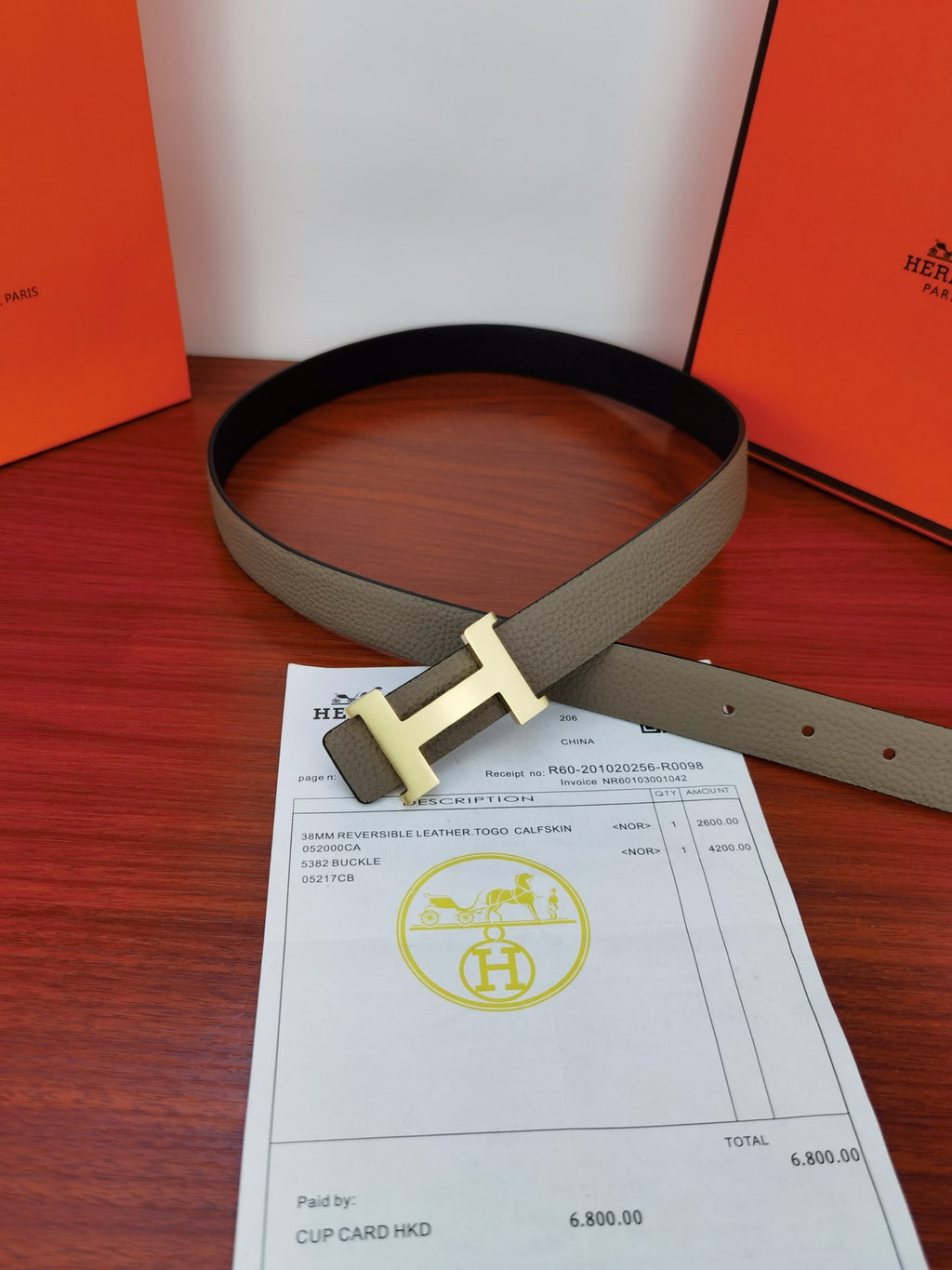 Hermes belt with light gray strap and gold-tone H buckle, laid flat