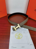 Hermes belt with light gray strap and gold-tone H buckle, laid flat