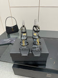 Black heeled sandals with gold chain logo detail, clear ankle straps