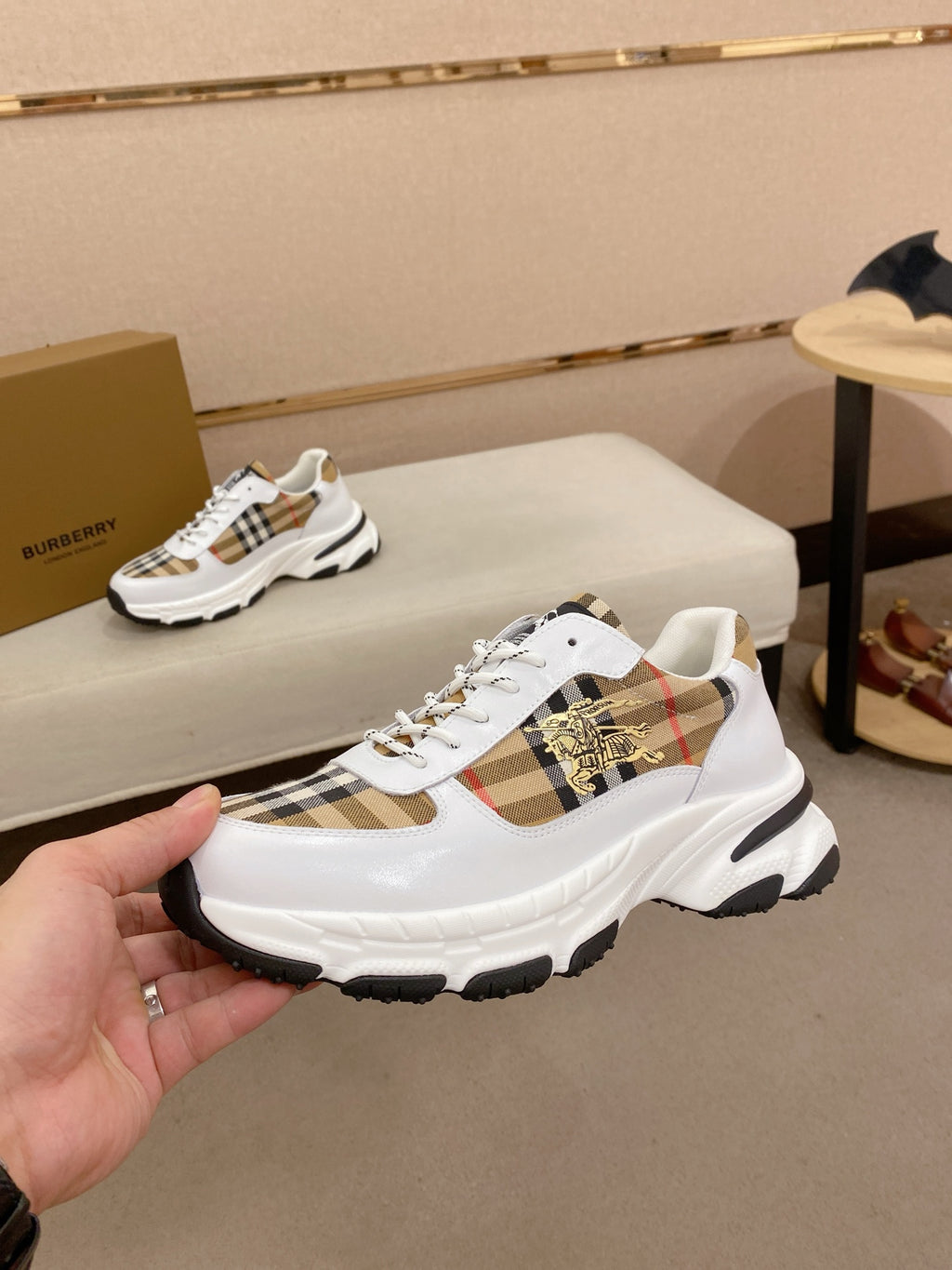 Burberry luxury sneakers on display, white uppers with check plaid and gold emblem