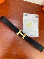 Hermes belt laid out: dark textured leather with gold-toned H buckle