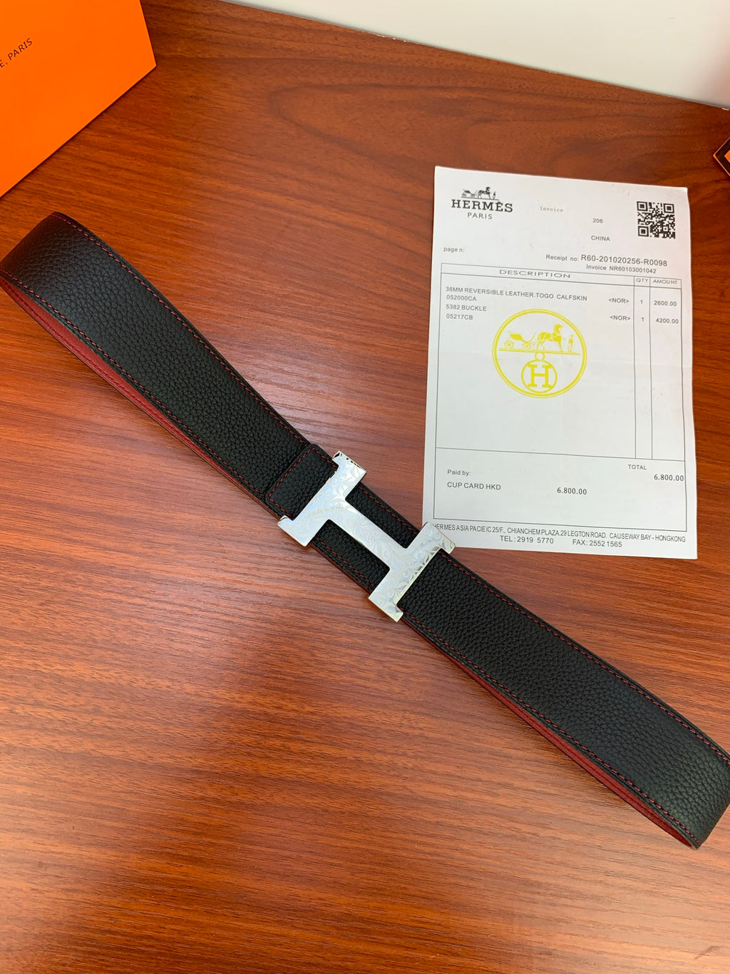 Hermes belt lying flat: black textured strap with gold buckle and red reverse