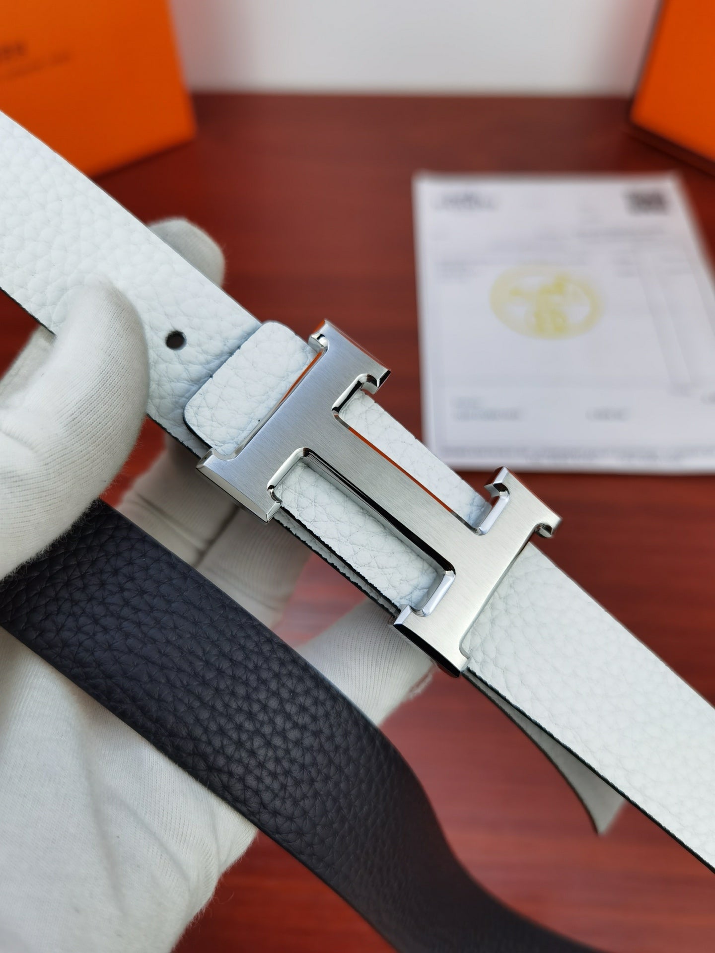 Hermes belt showing reversible dark side with silver buckle on light leather strap