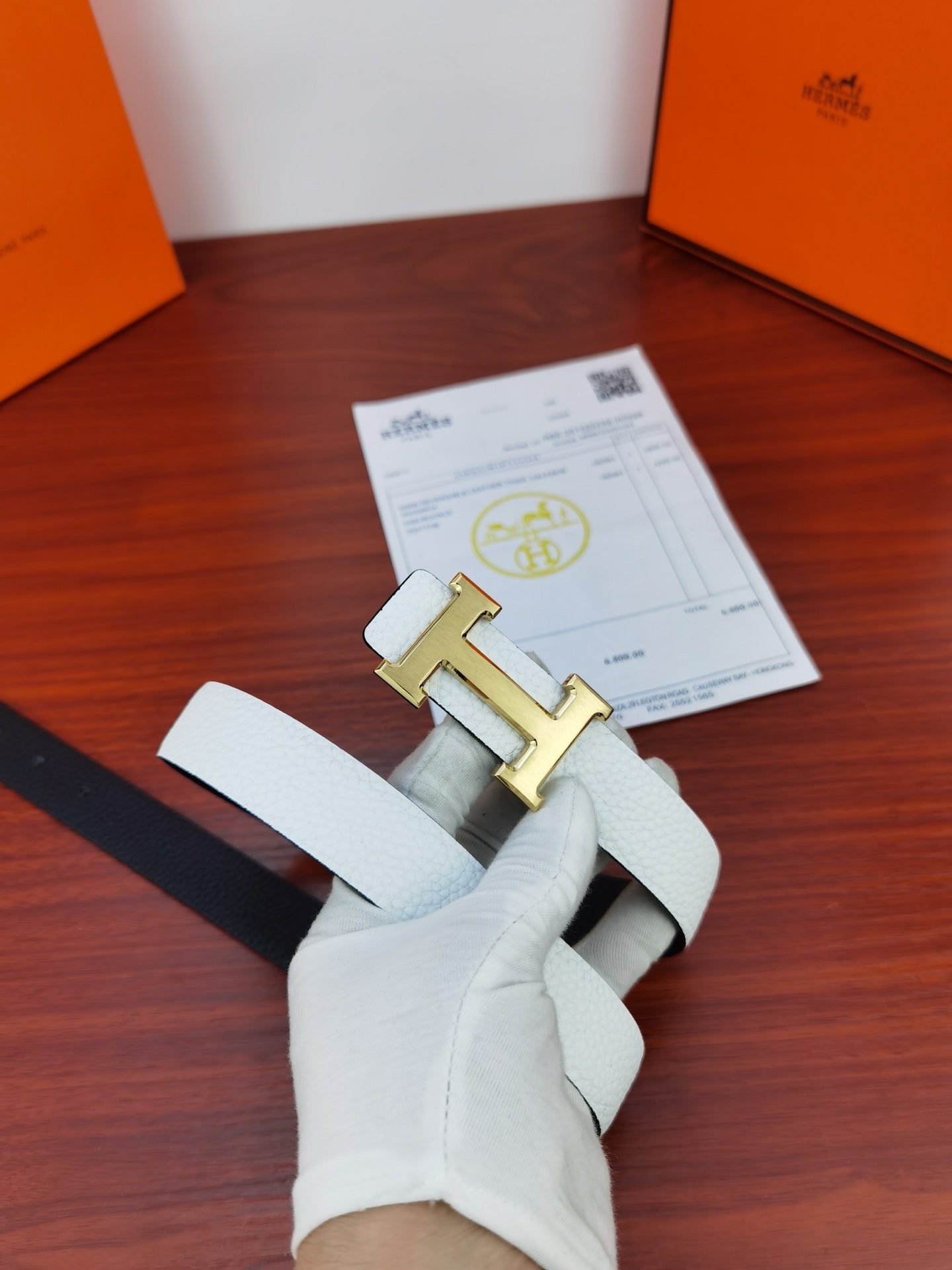 Hermes belt on hand with light white strap, silver buckle, and punched holes