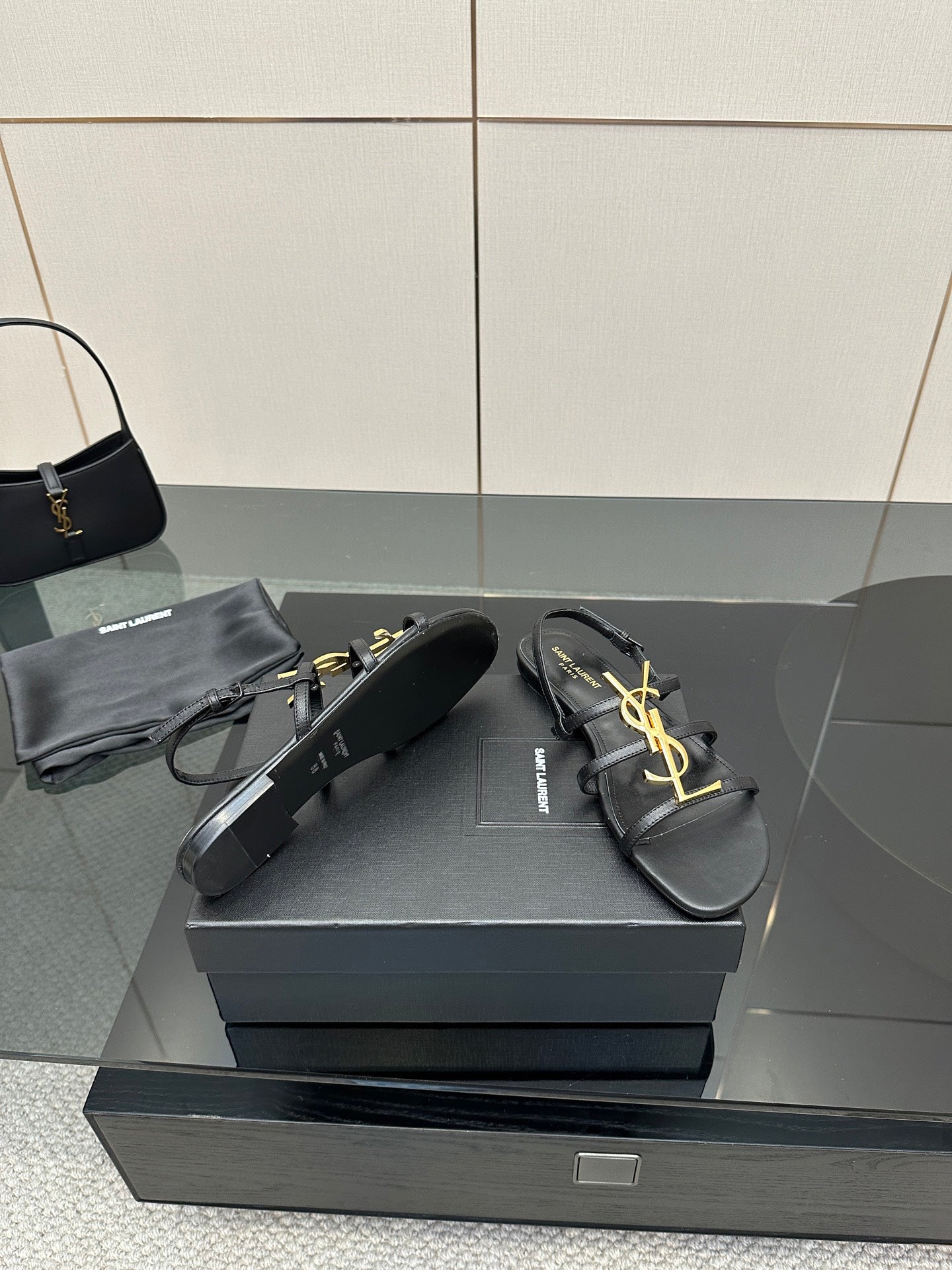 Black leather thong sandals with gold YSL logo, placed on a box