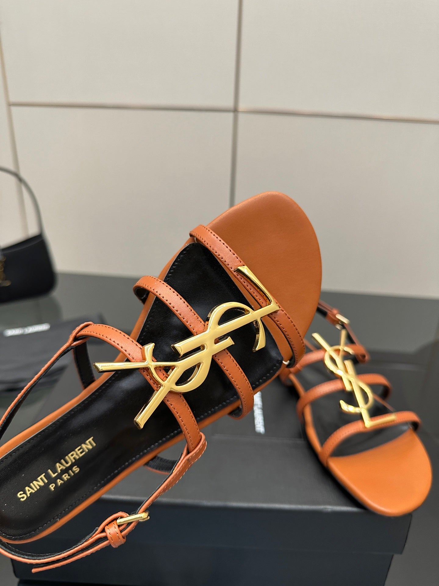 Women's sandal close-up: orange straps over black footbed with SAINT LAURENT logo detail