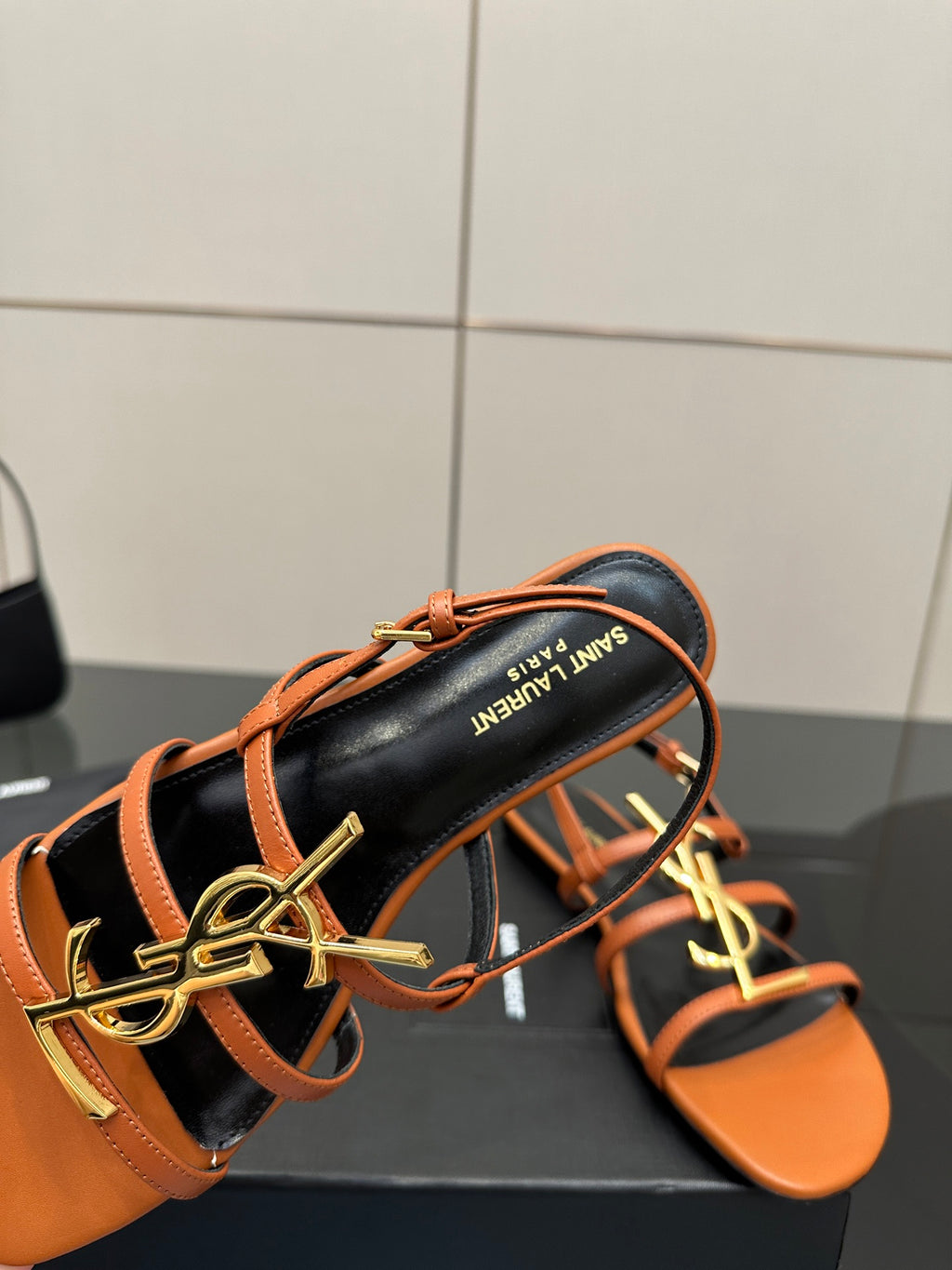 Women's sandal close-up: black footbed with orange straps and gold-tone SAINT LAURENT logo