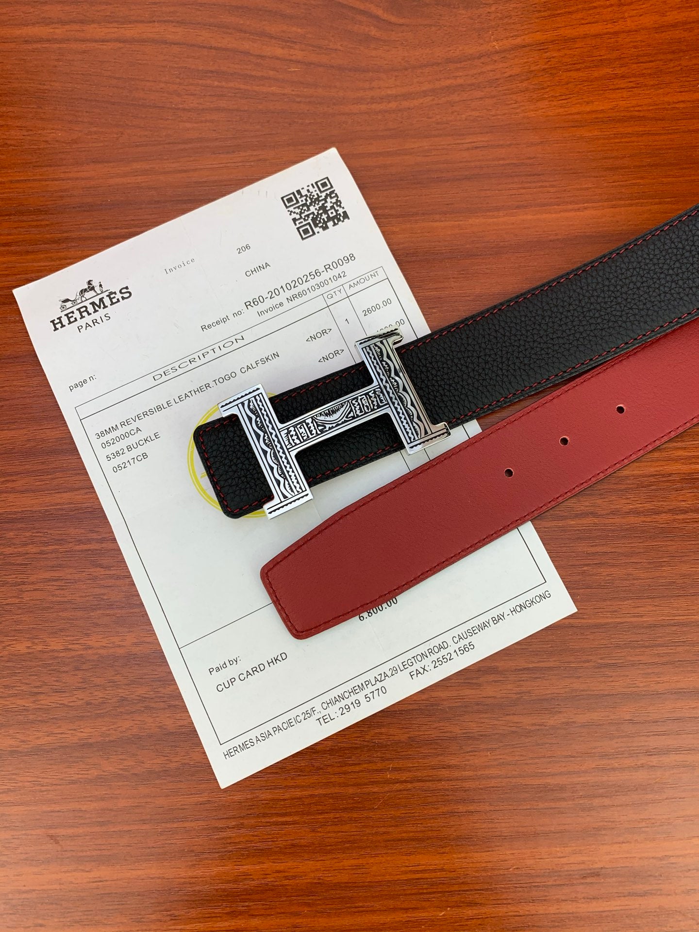 Hermes belt showing black textured strap and red leather underside with silver H buckle