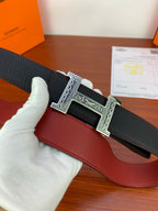 Hermes belt detail: black textured strap with silver engraved H buckle over red leather panel