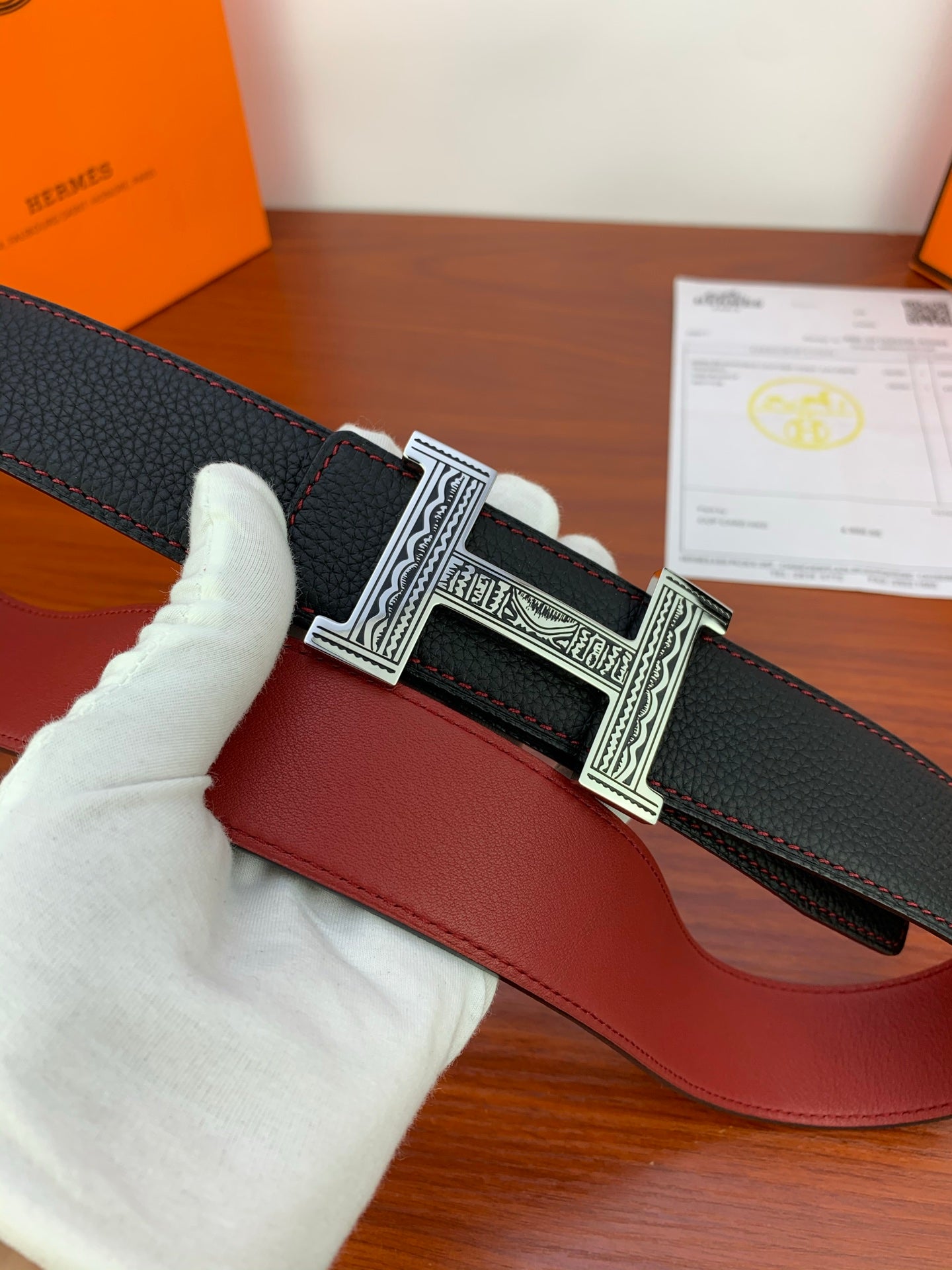 Hermes belt detail: black textured strap with silver engraved H buckle over red leather panel