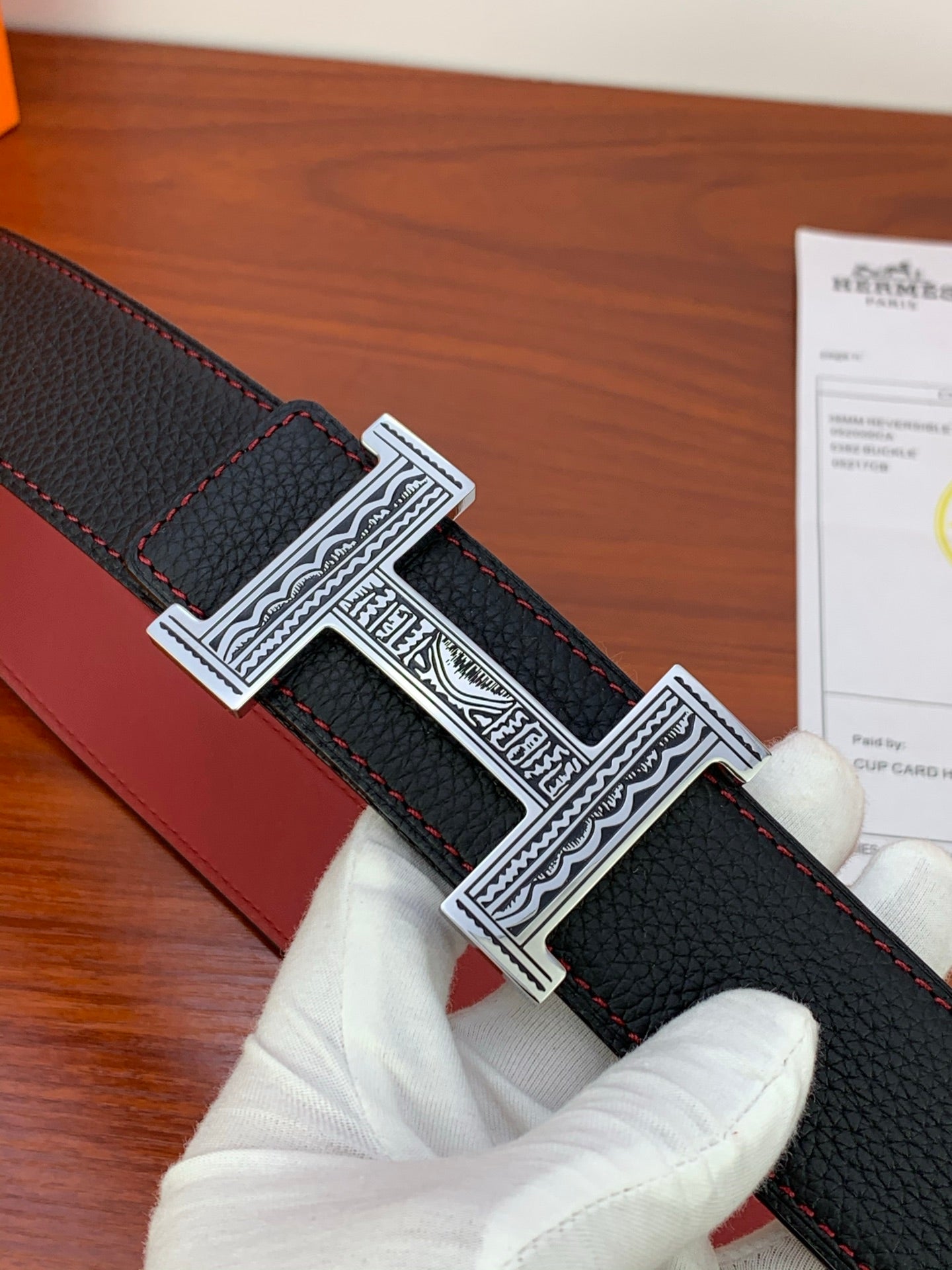 Hermes belt detail with silver engraved H buckle on black textured leather, red underside