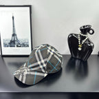 Burberry cap in dark gray, white, and blue plaid with crest emblem on the front panel.
