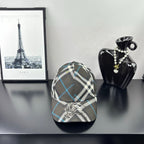 Burberry cap in dark gray, white, and blue plaid with crest emblem on front.
