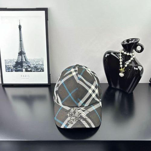 Burberry cap in dark gray, white, and blue plaid with crest emblem on front.