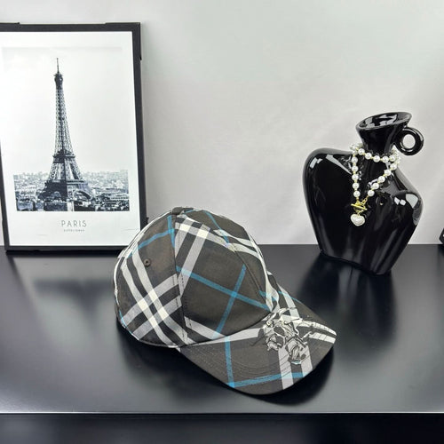 Burberry cap in dark gray, white, and blue plaid with crest emblem and curved brim.