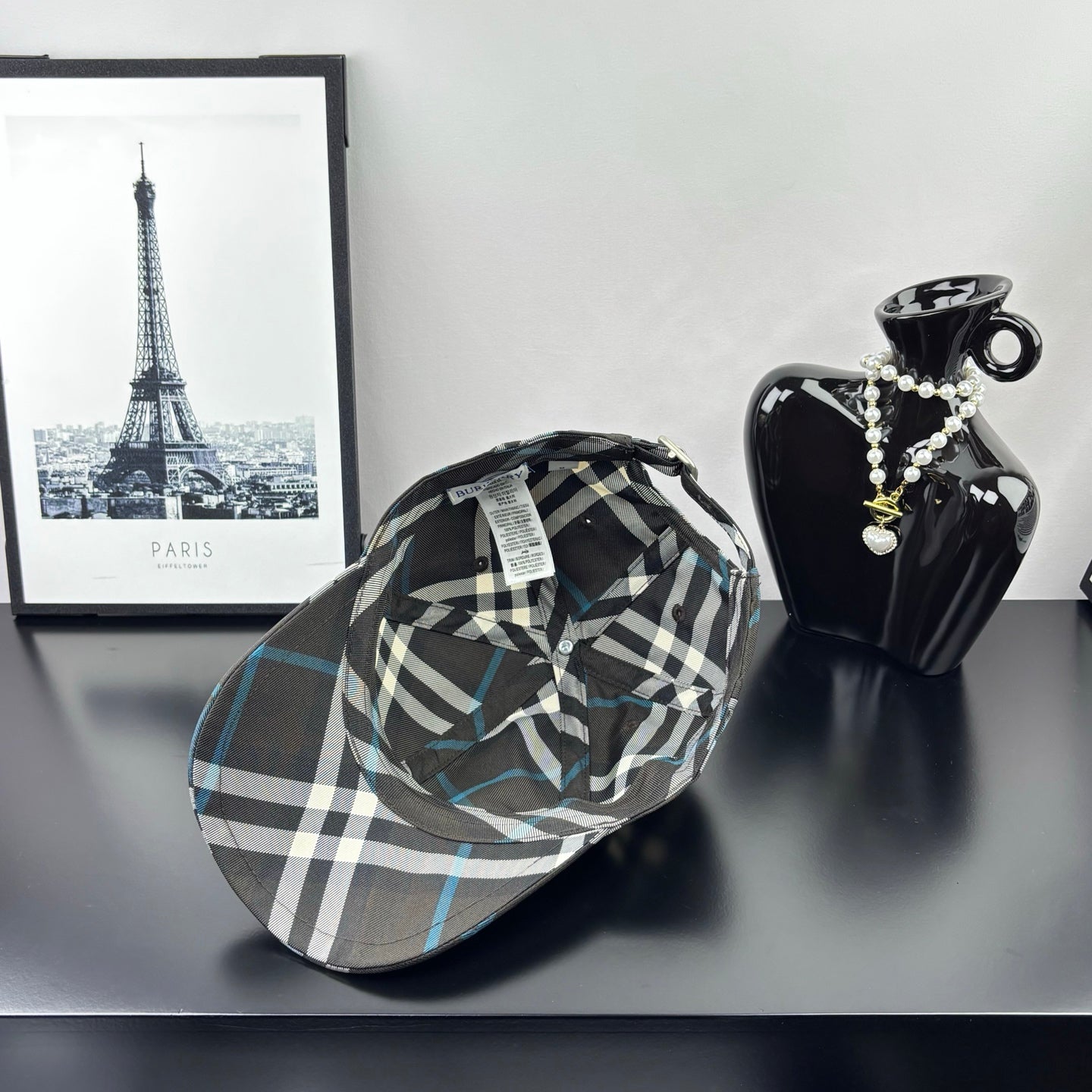 Burberry cap in dark gray and blue plaid with crest emblem near the front.