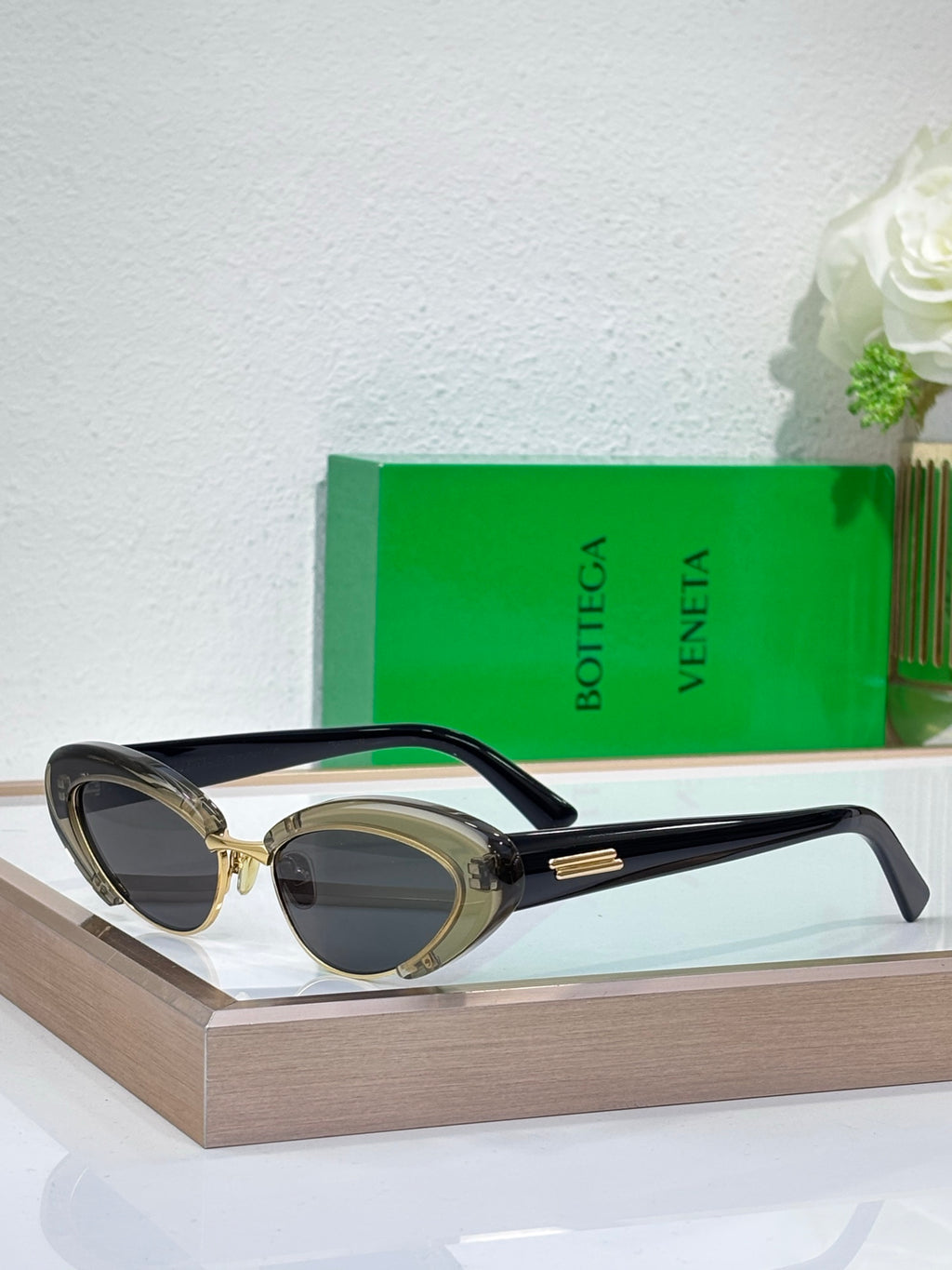 Bottega Veneta sunglasses with black frames, gold-tone details, and oval dark lenses
