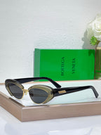 Bottega Veneta sunglasses with black frames, gold-tone details, and oval dark lenses