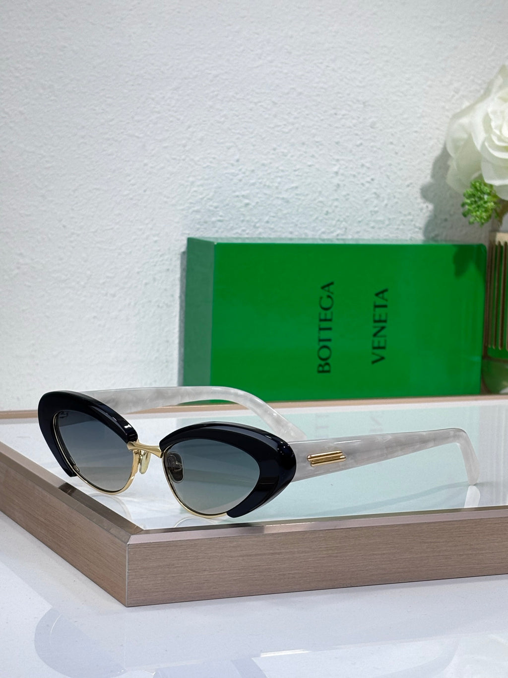 Bottega Veneta sunglasses with clear frames, dark tinted oval lenses, and gold accents