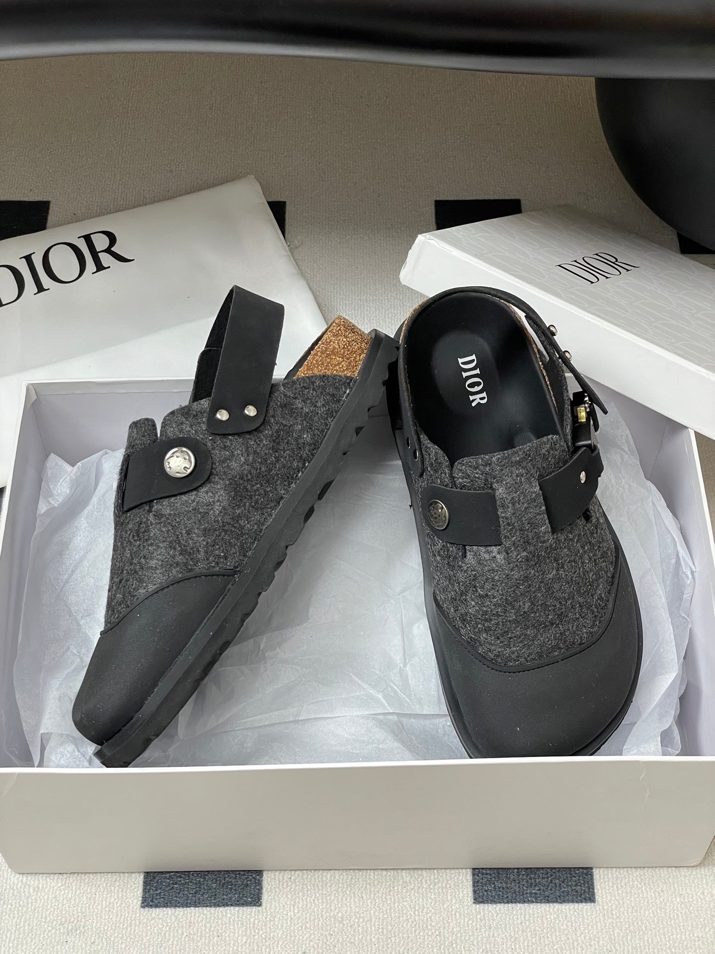 Dior mule sandals with gray speckled upper, black strap, round emblem, and gold studs