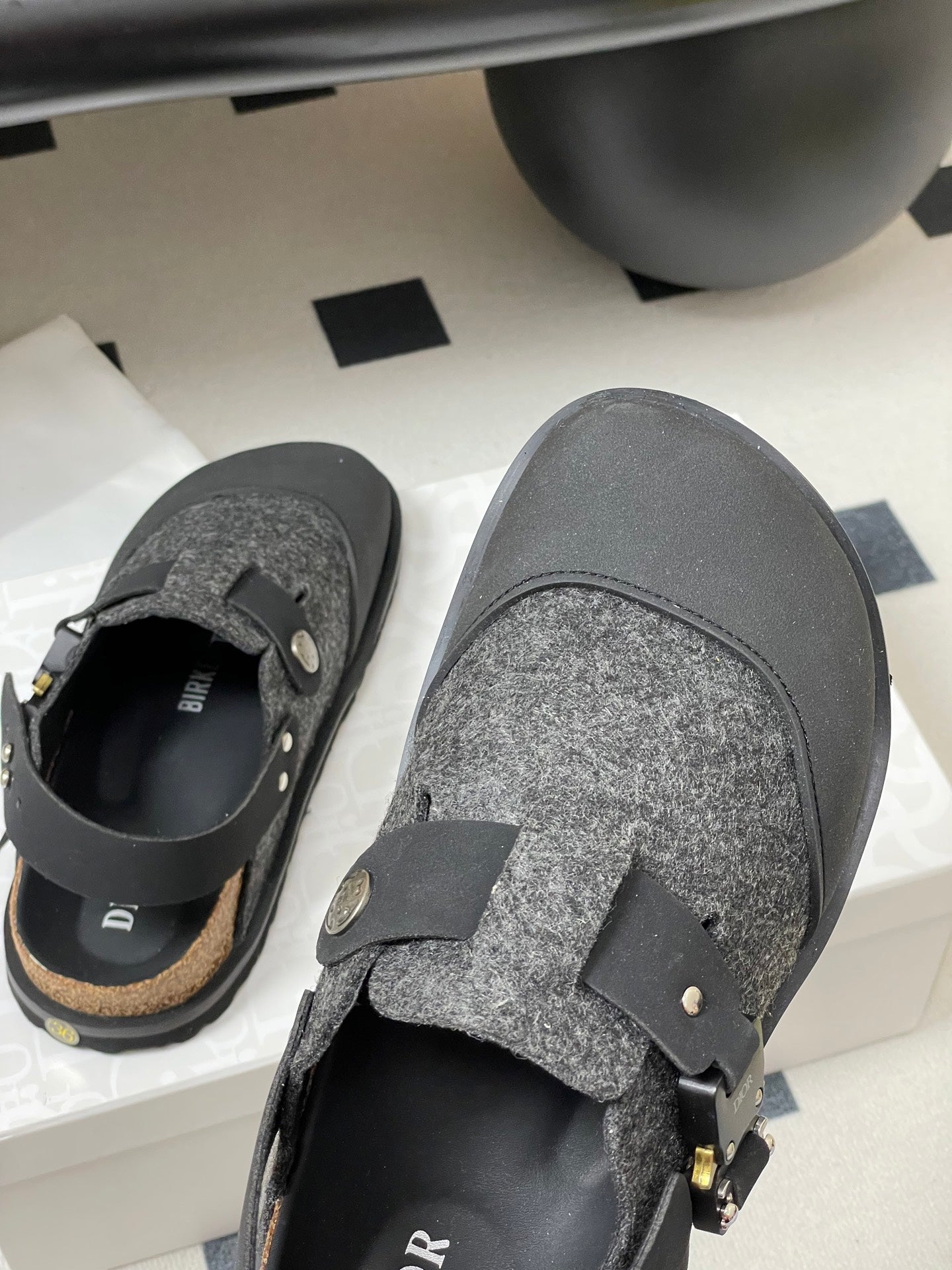 Dior sandals close-up with gray textured upper, black strap, and gold-toned buckle detail