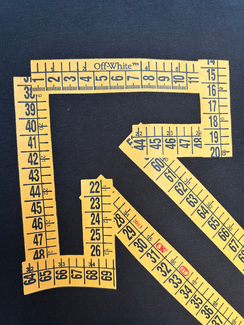 Dark T-shirt graphic detail: yellow ruler-tape arrow X