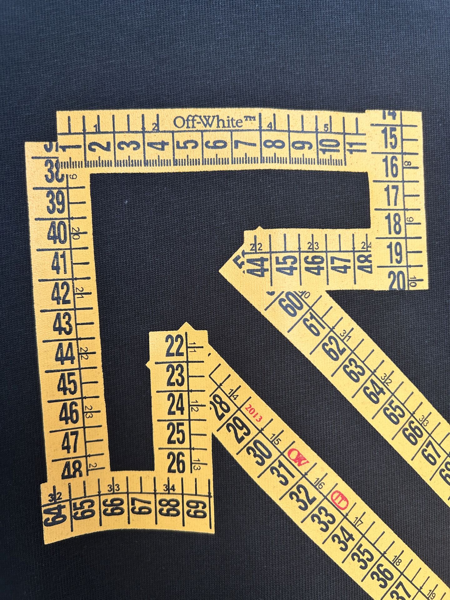 Dark T-shirt closeup showing yellow ruler markings and arrow graphic detail