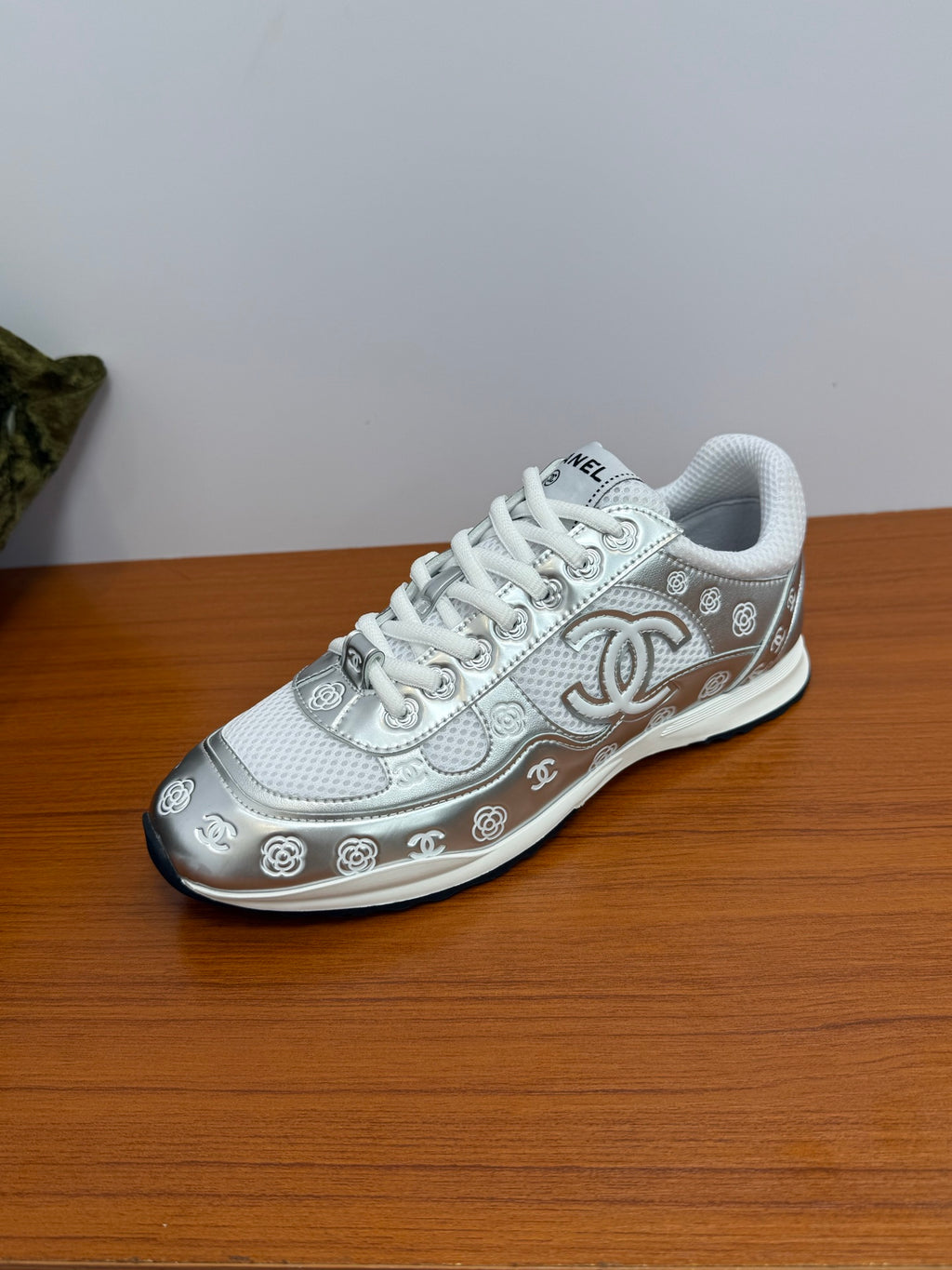 Chanel white low-top sneaker, angled view with large logo emblem and patterned side.