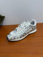 Chanel white low-top sneaker, angled view with large logo emblem and patterned side.