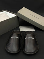 Black leather slides, BALENCIAGA logo print on footbed, side-by-side