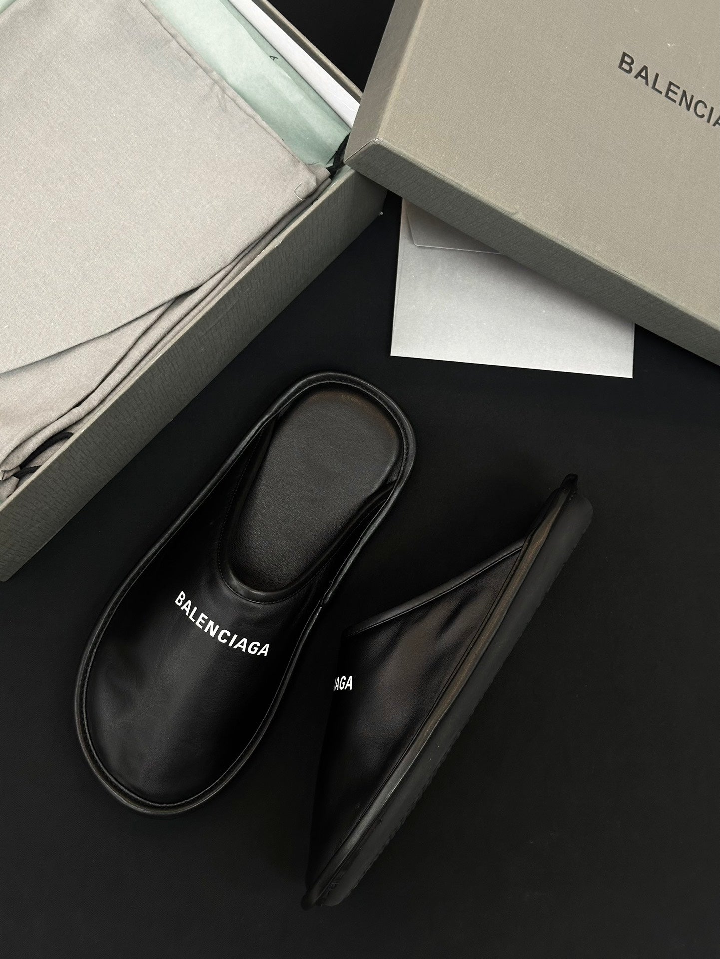 Black leather slides with BALENCIAGA logo on insole, angled pair