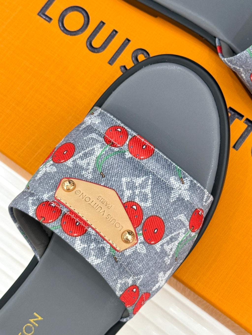 Women’s slide sandals close-up: blue cherry-print denim strap with tan logo patch