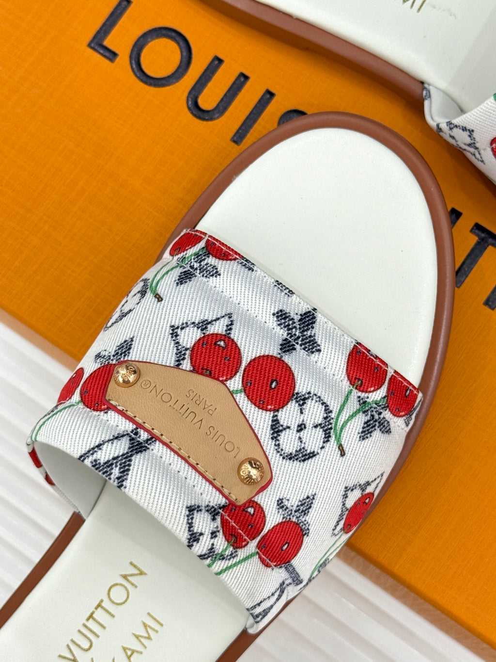 Ladies slide sandal showing white cherry-print strap with gold logo patch