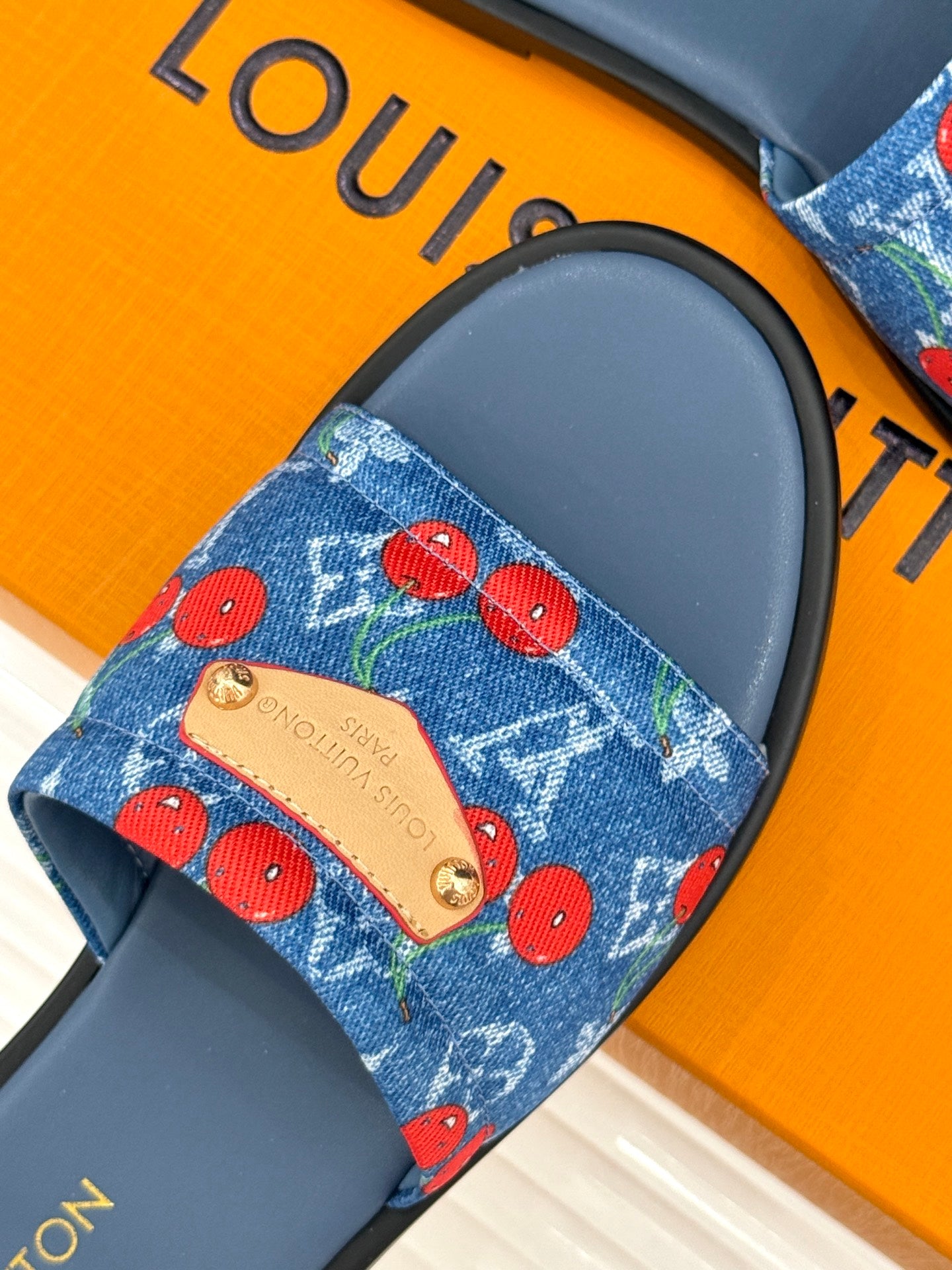 Louis Vuitton denim slide strap with red cherries and gold logo plaque on blue