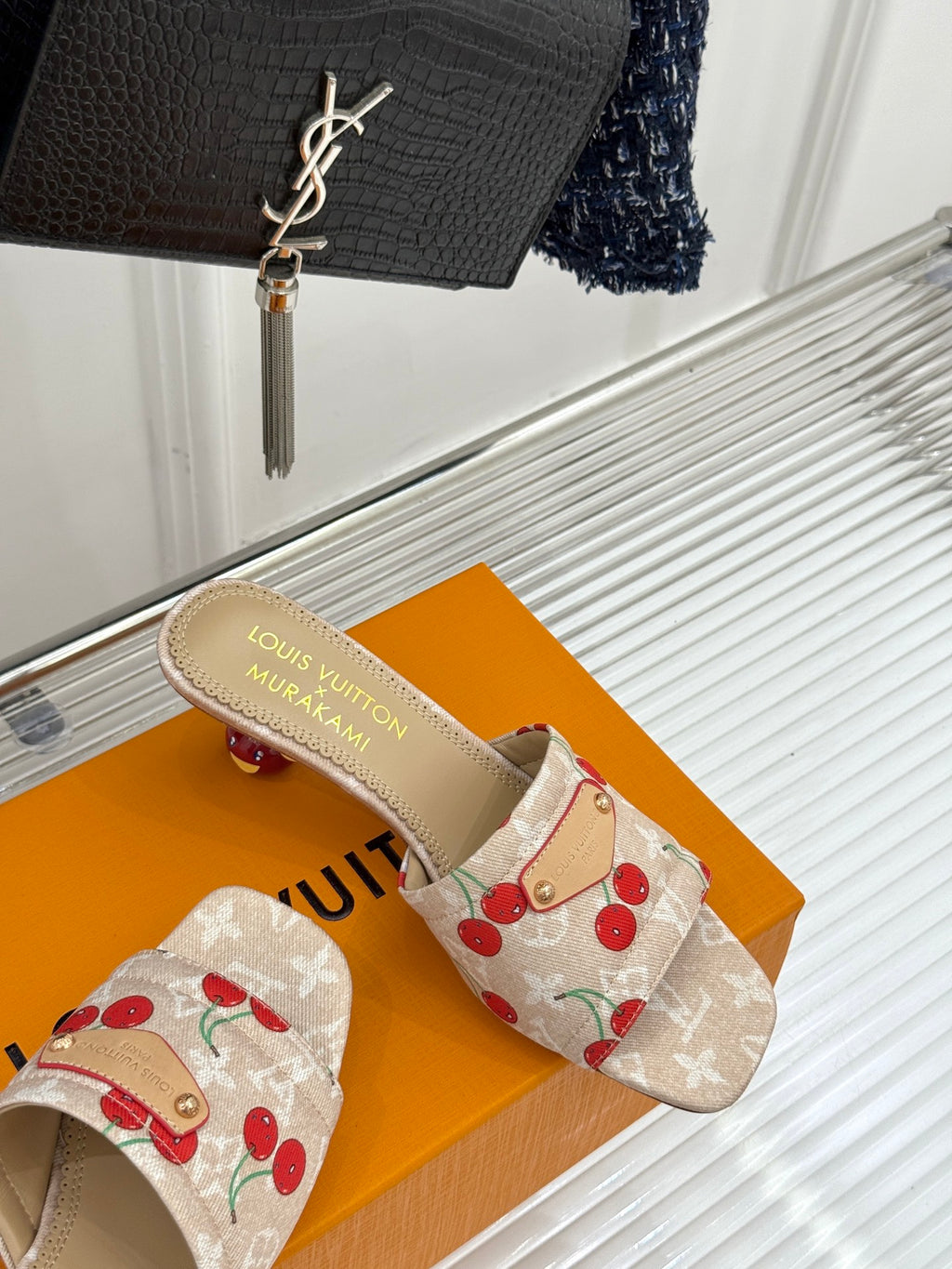 Beige cherry-print mule sandals with gold-tone logo footbed and fabric strap.