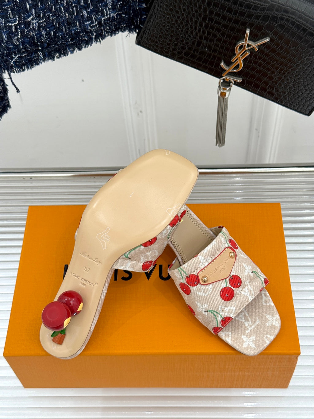 Beige cherry-print slide mule sandals with low heel and gold-tone buckle.