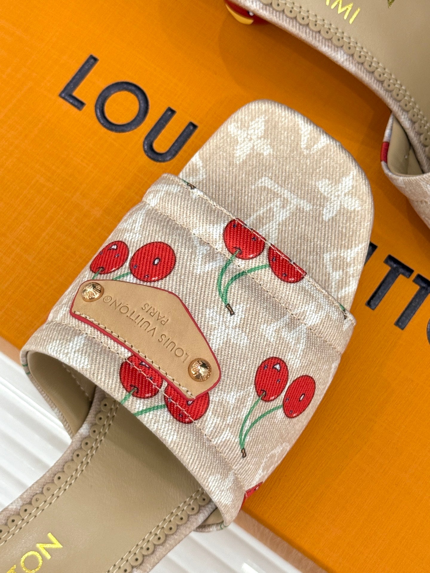 Close-up of beige cherry-print mule sandal strap with gold buckle details.