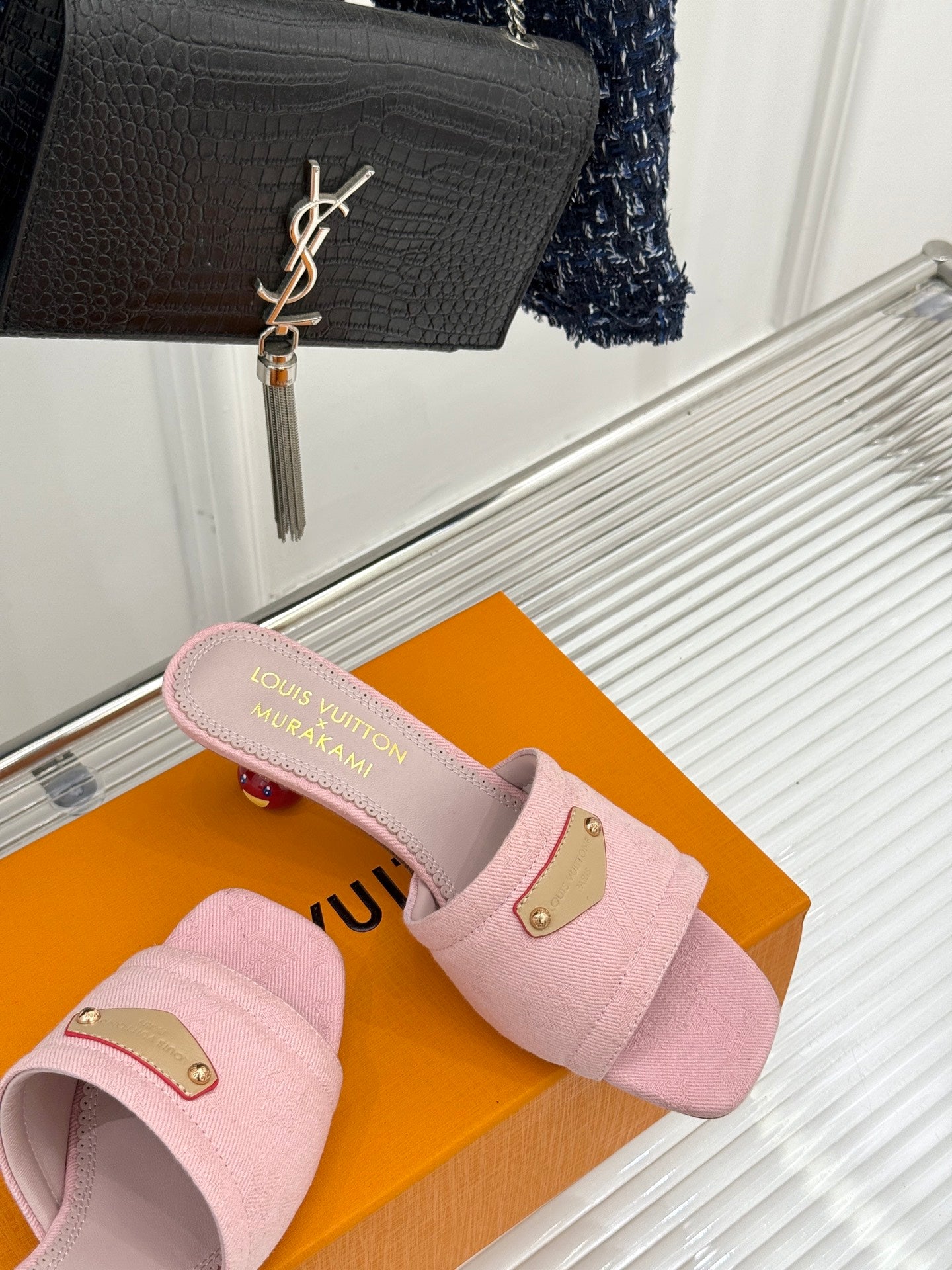 Pink slide sandals with gold buckle plates, side view on orange box