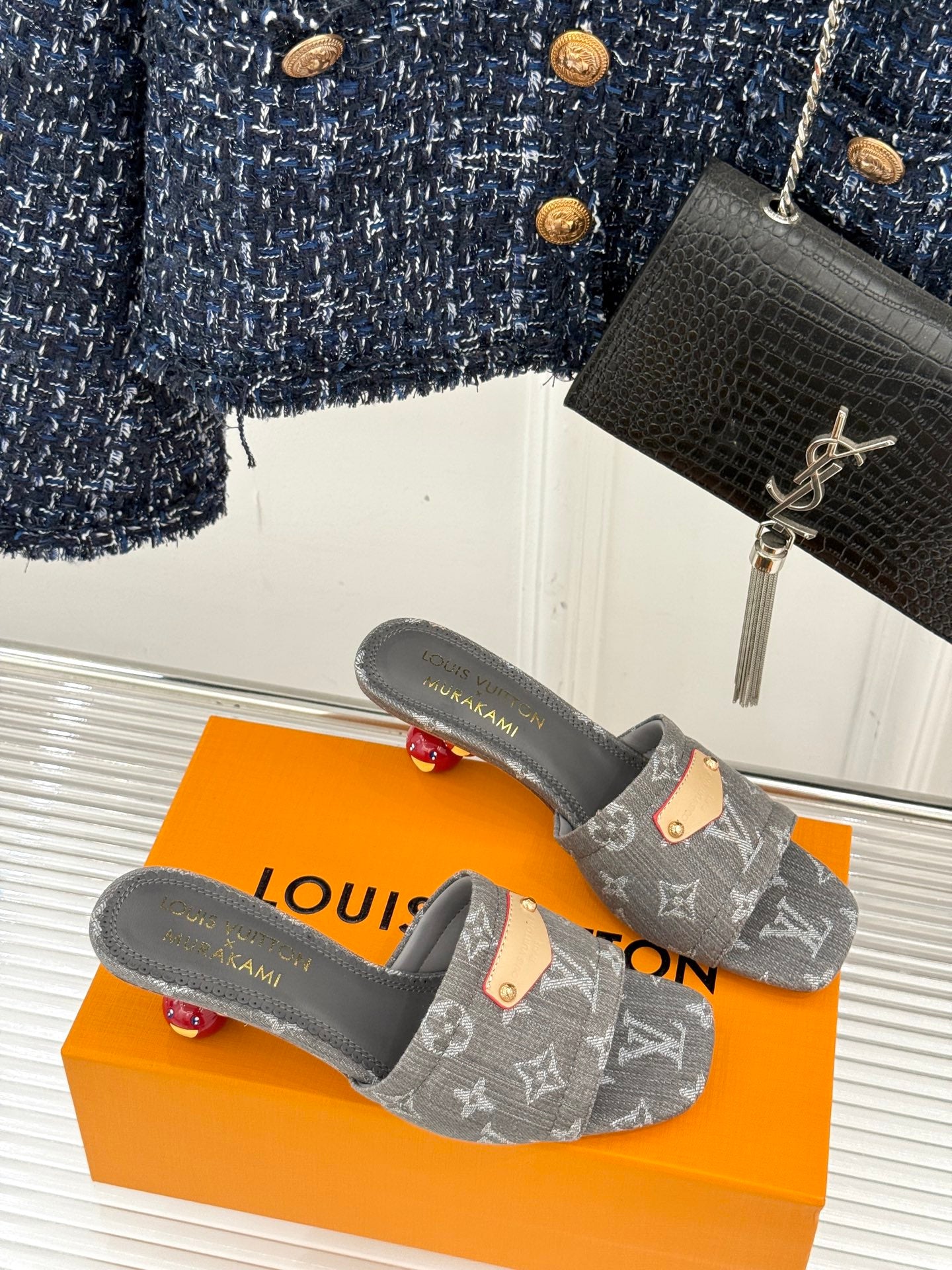 Women's gray monogram mule slides on orange box, tan buckle accent at front