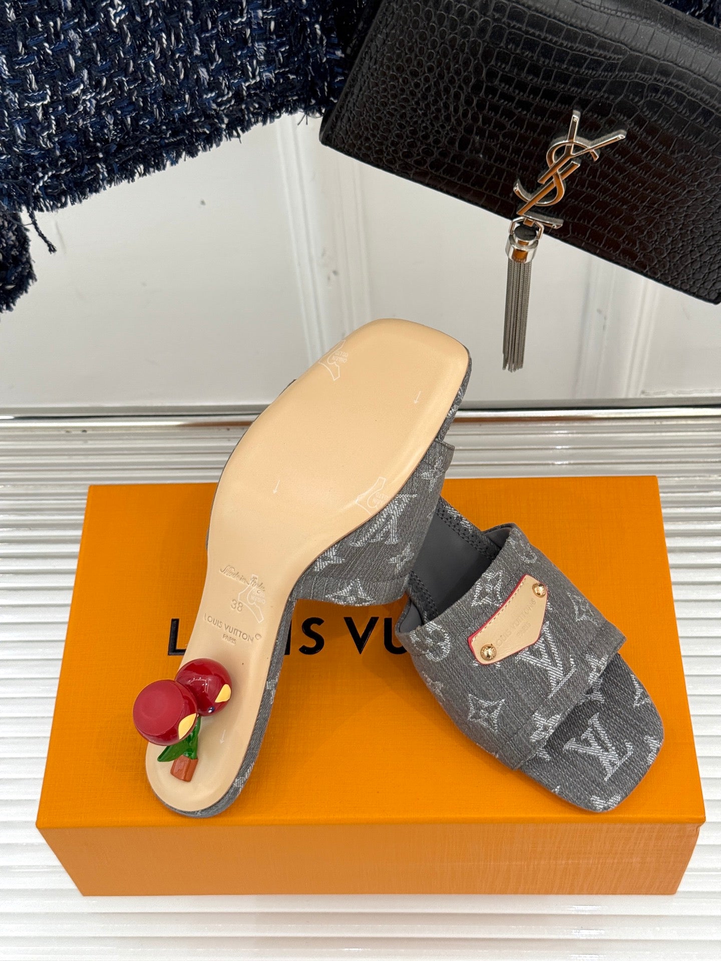 Women's gray monogram mule slides with tan buckle detail on orange box