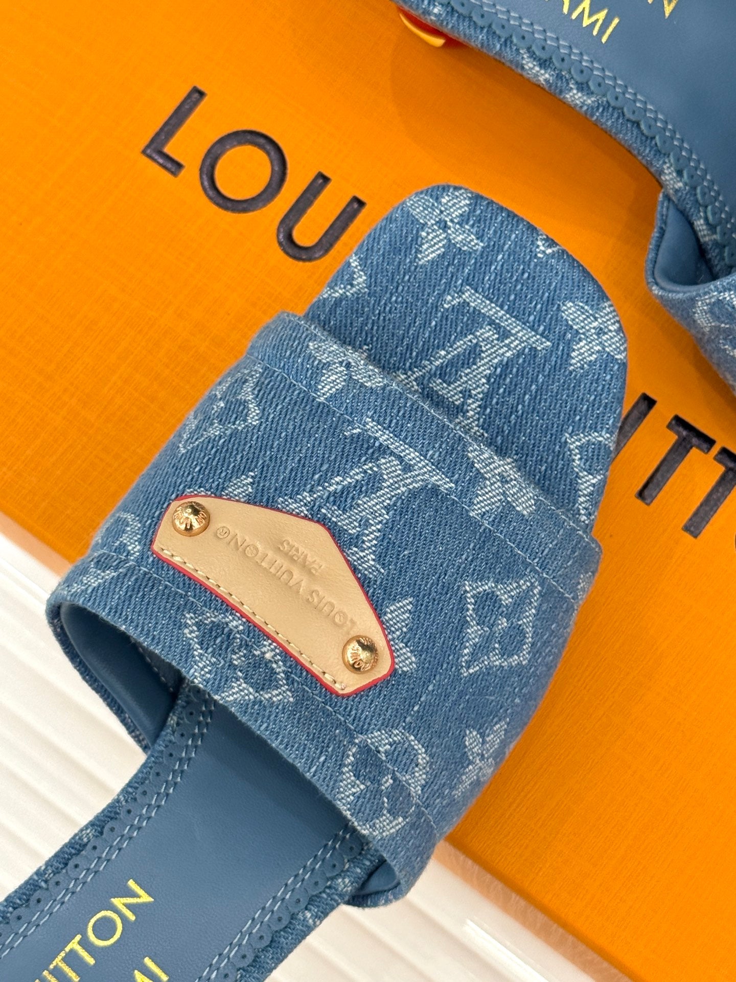 Close-up: blue Monogram slide sandal with tan logo patch and stitched straps