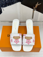 Pair of white slide sandals with pink flower print and gold buckle straps