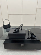 Black leather open-toe mules with gold detail and stiletto heels on display box