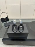 Black leather slide mules with open toe, gold accent, and stiletto heels