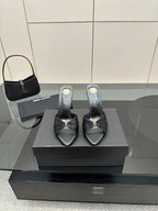 Black leather slide mules with open toe, gold accent, and stiletto heels