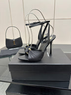 Black strappy stiletto heeled sandals with thin heel and ankle wrap, on box